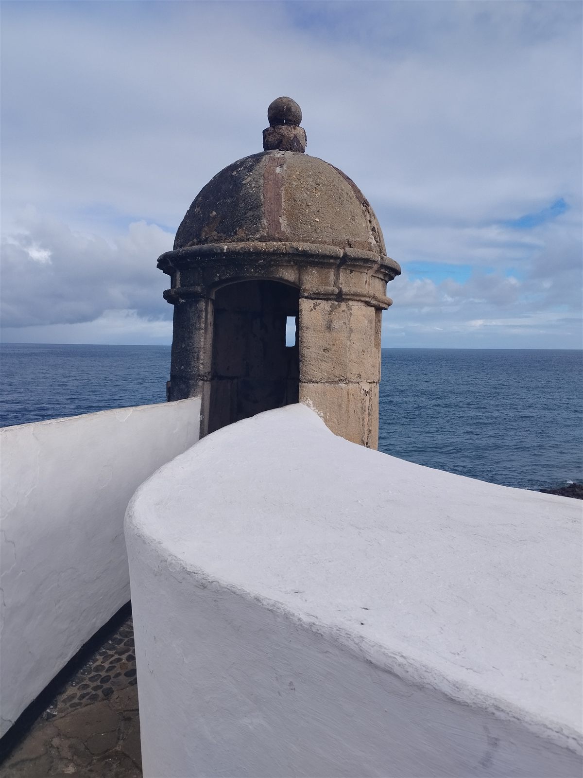 Stone lookout above the sea, framed by curved white walls beneath a cloudy sky